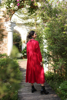 Woman in a red dress standing on a wooden path surrounded by greenery and flowers.