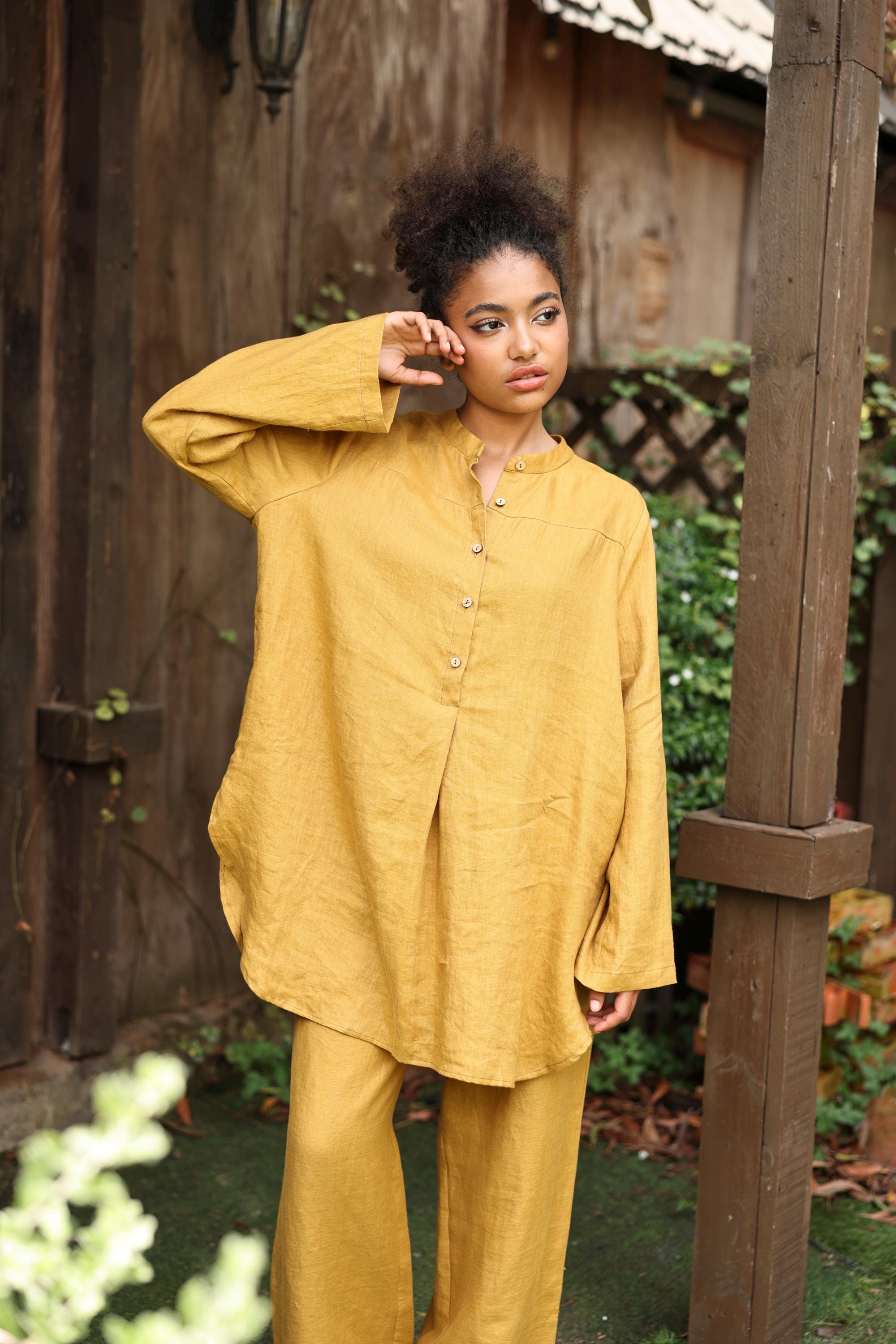 Woman wearing a yellow outfit standing outdoors near a wooden structure.