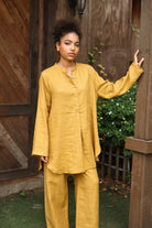 Woman wearing a mustard yellow outfit standing against a wooden background