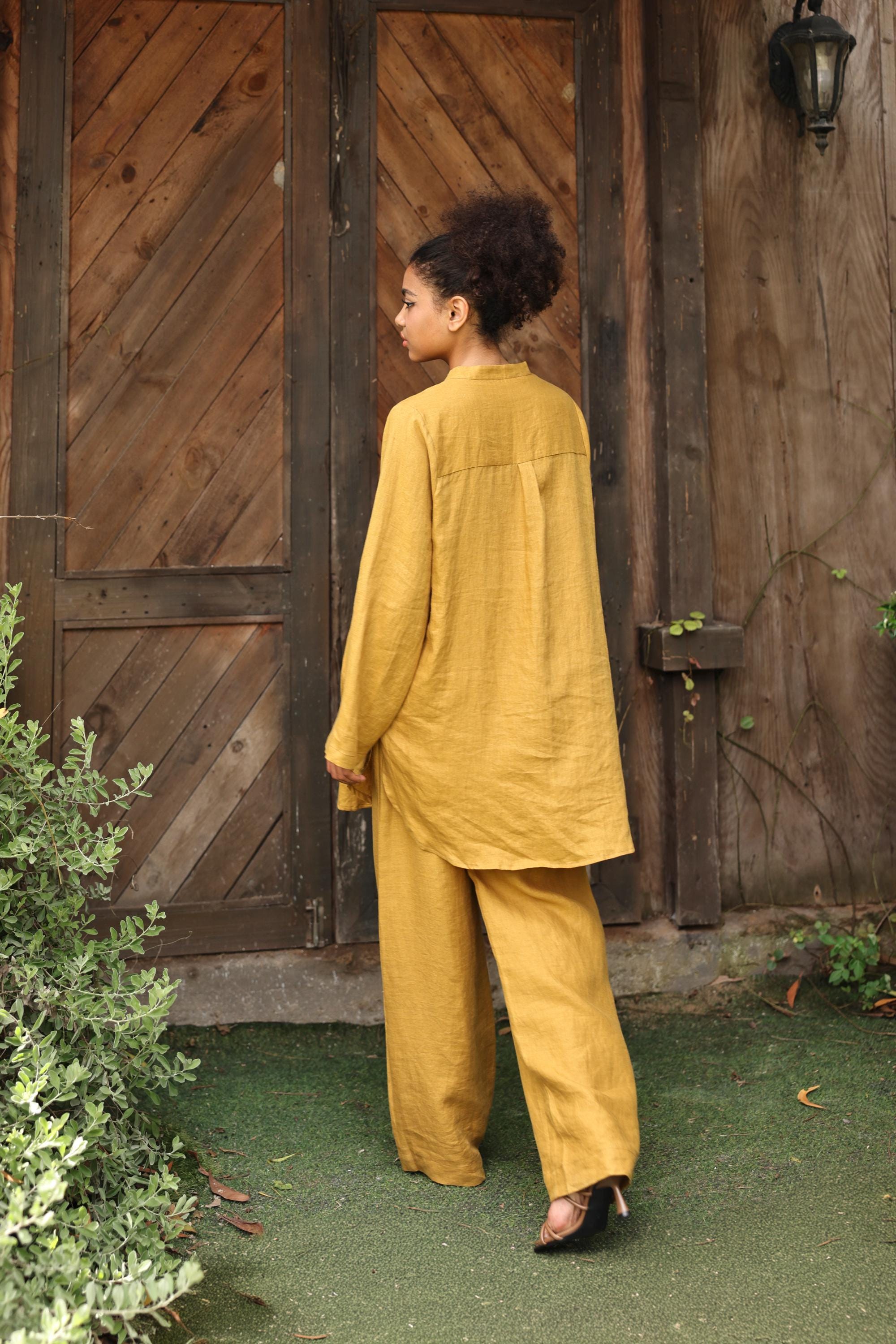 Woman in mustard yellow outfit standing in front of a wooden door.