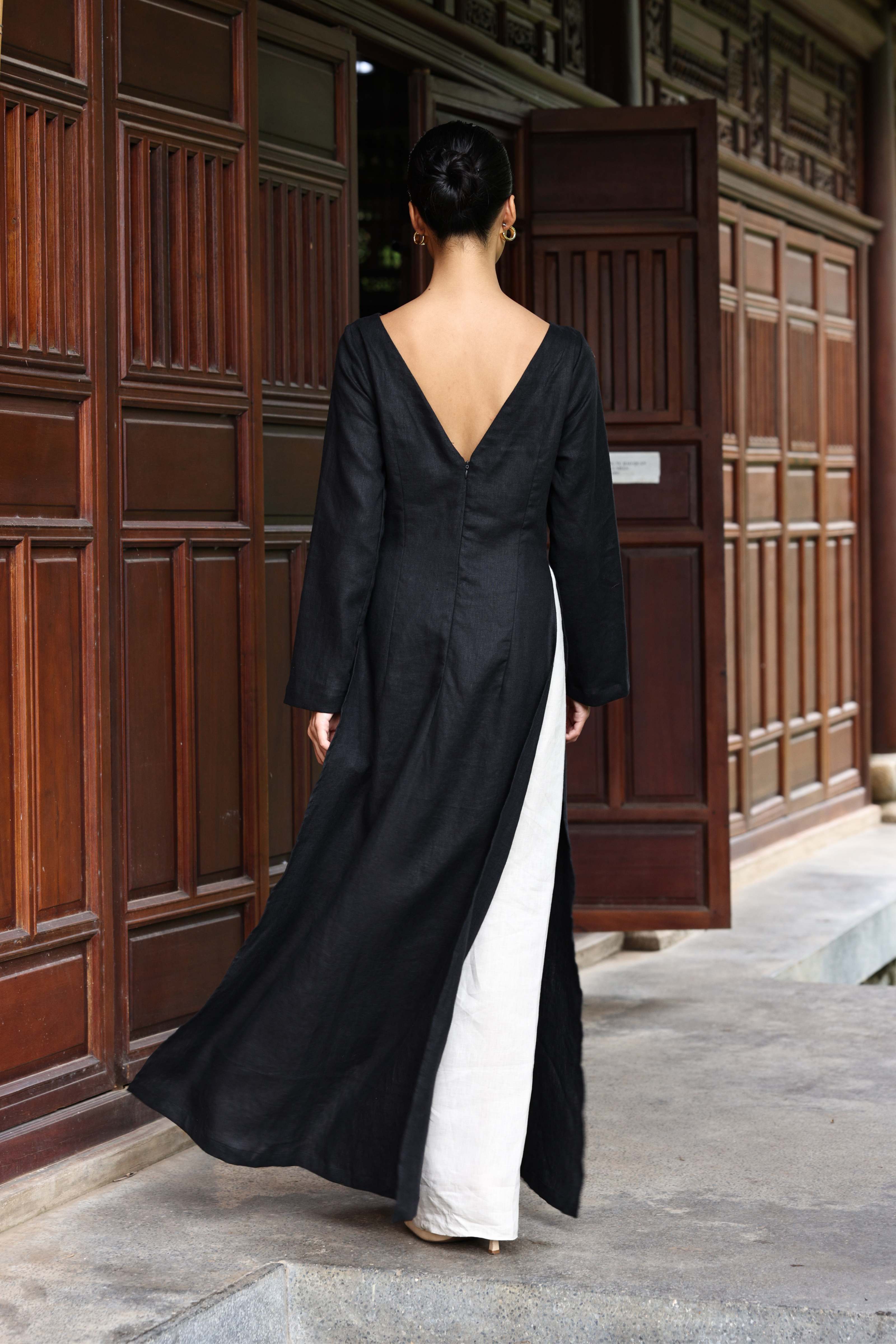 Woman in a black tunic and white pants standing in front of a wooden door.