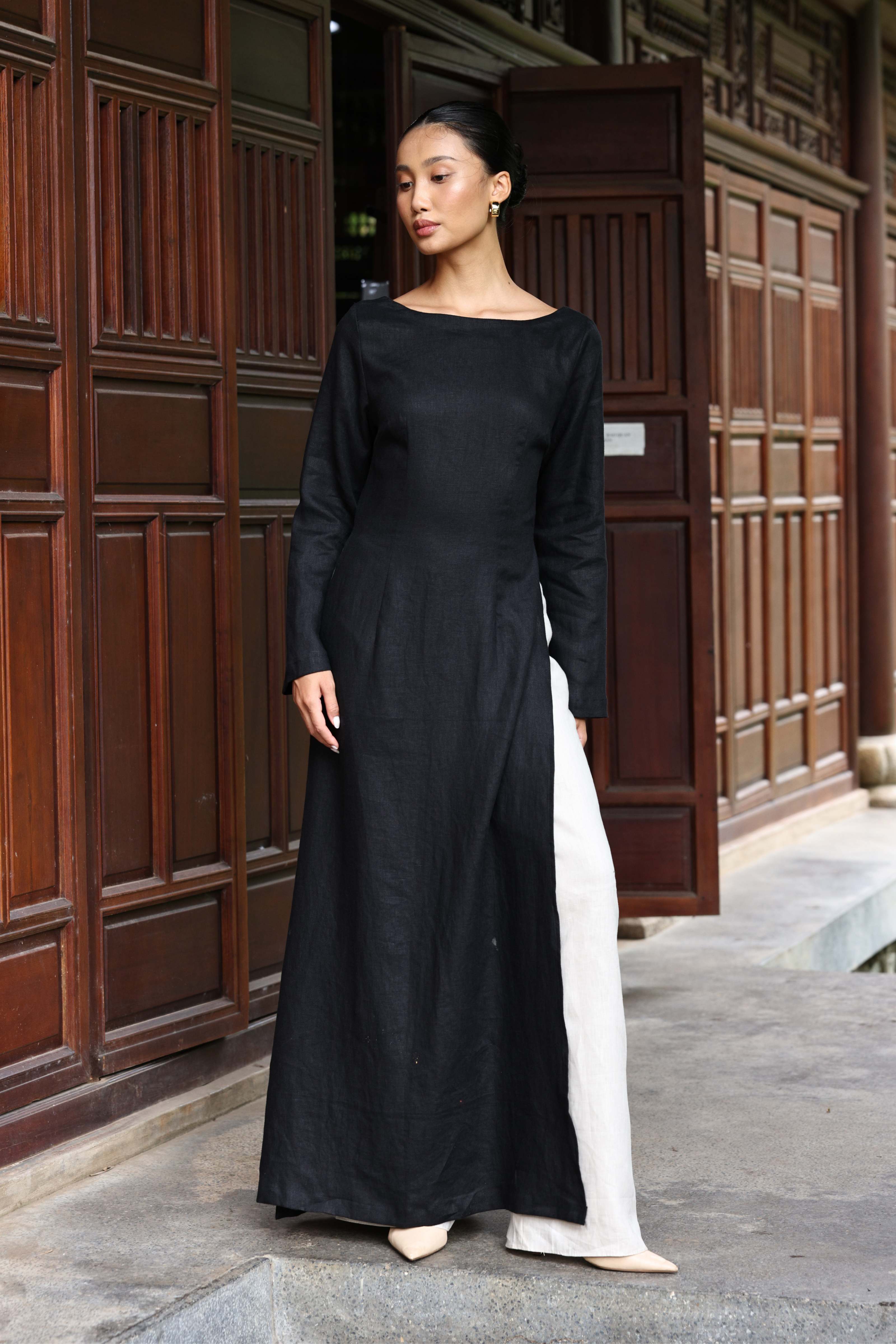 Woman wearing a black long-sleeve dress standing in front of a wooden door.