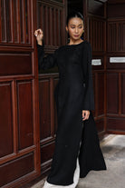 Woman in a black outfit standing in a room with wooden paneling.