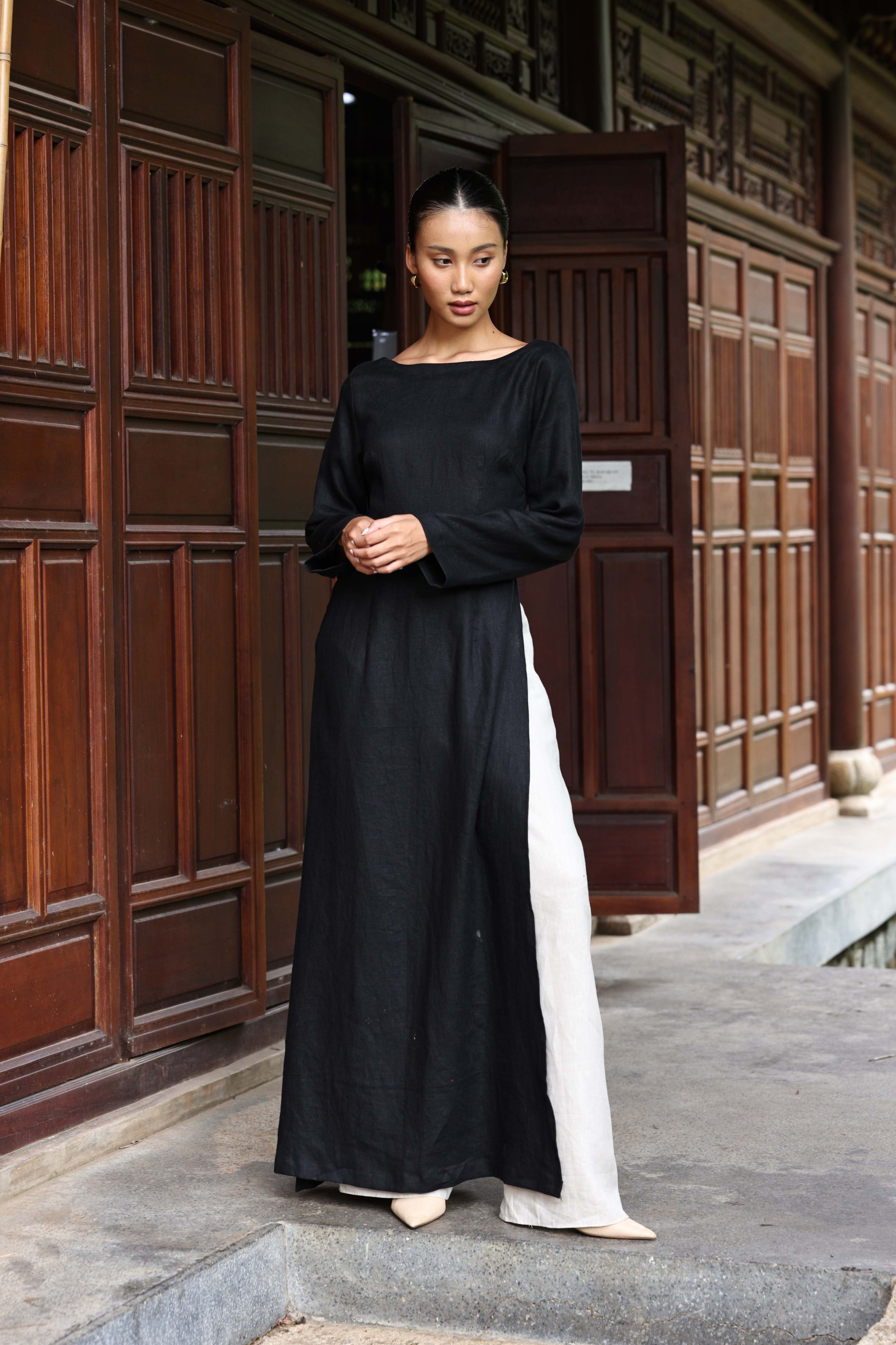 Woman wearing a black tunic and white pants standing in front of wooden doors.