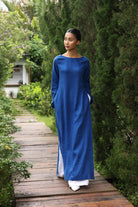 Woman in a blue dress standing on a wooden path surrounded by greenery