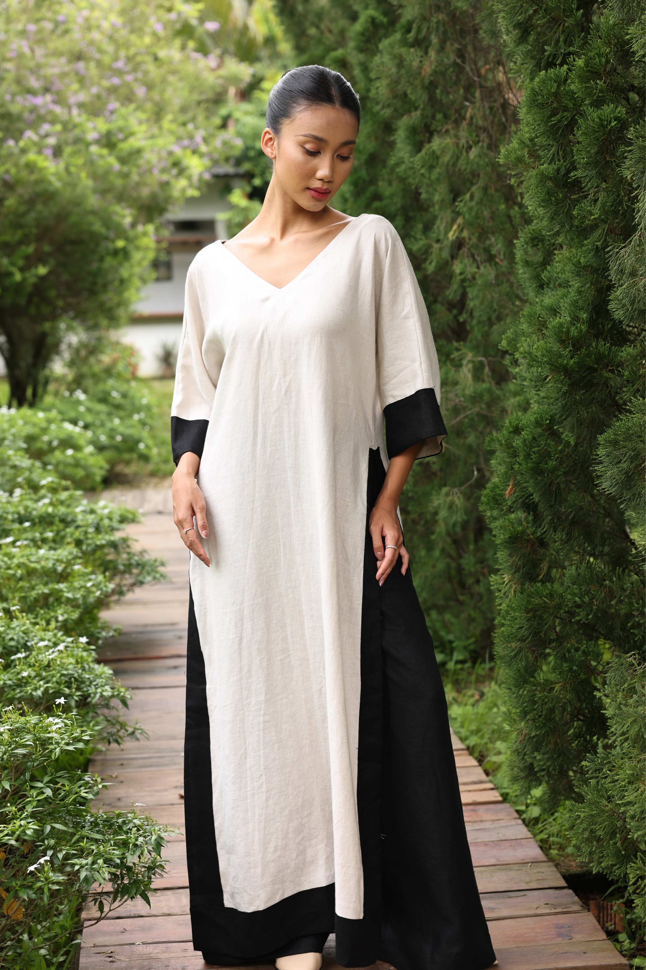 Woman wearing a black and white dress walking on a wooden path in a garden.