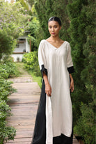 Woman wearing a long, light-colored dress with black accents in a garden setting
