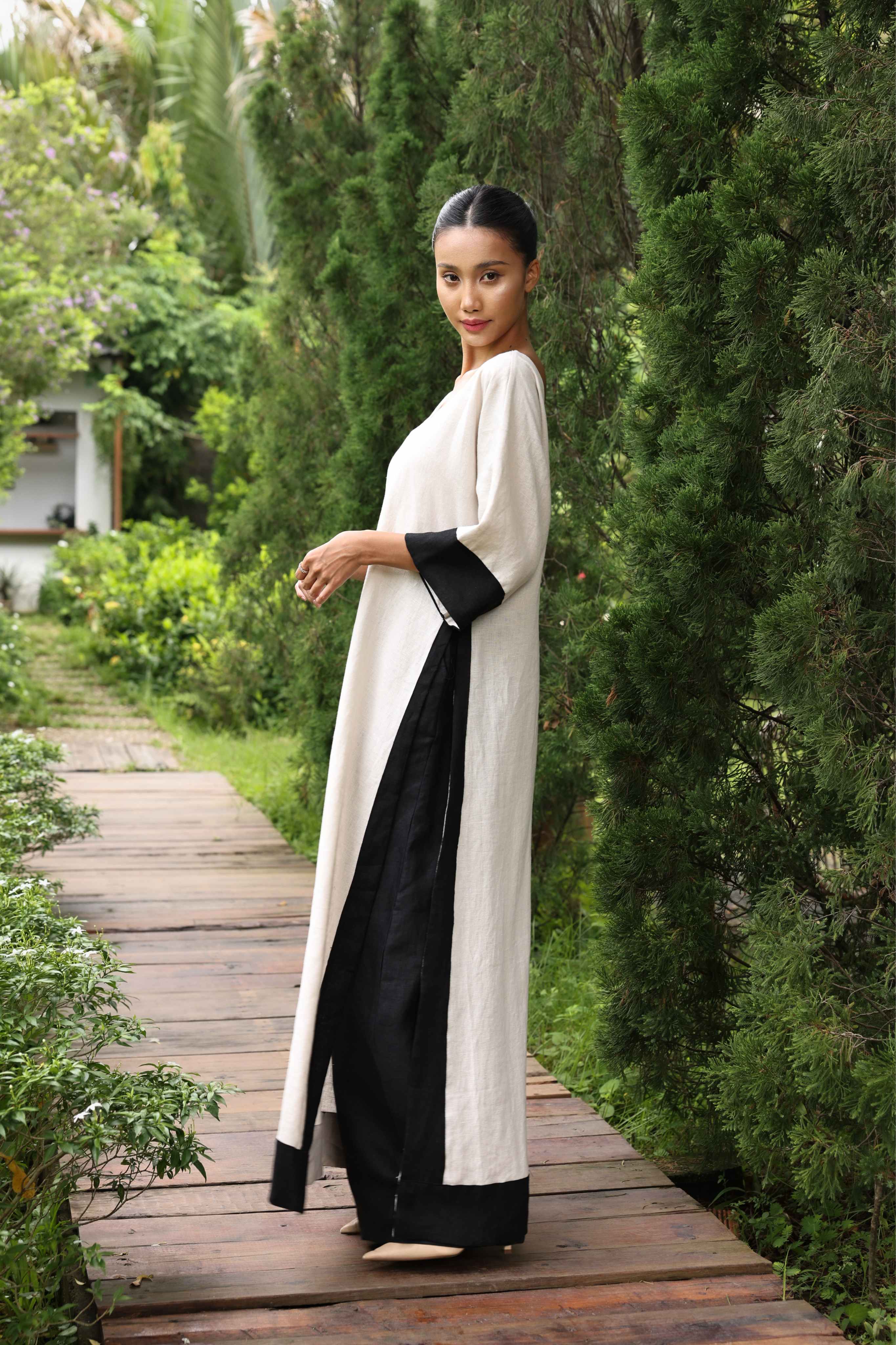Woman in a black and white dress standing on a wooden path surrounded by greenery