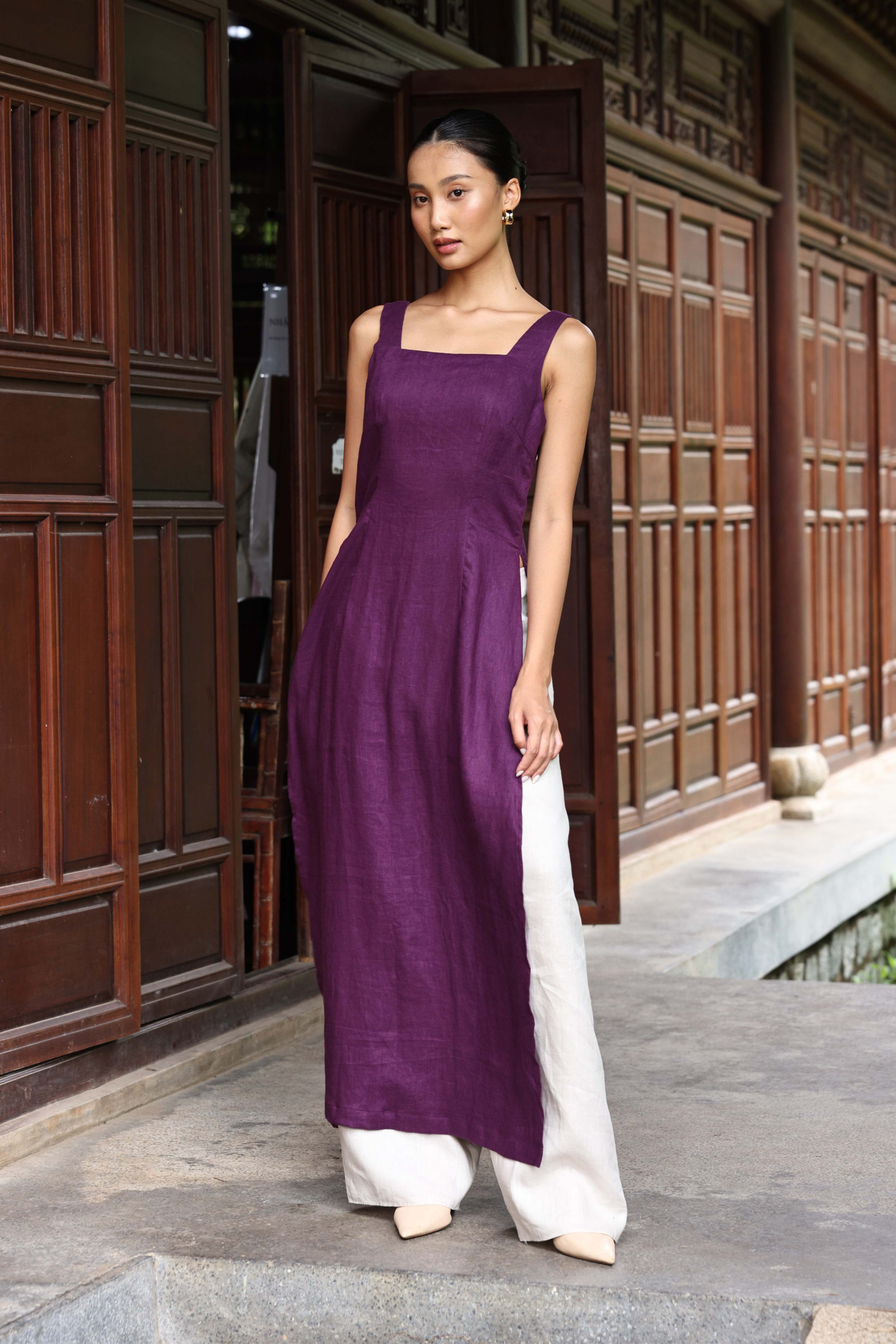 Woman wearing a long purple dress with white pants standing in front of wooden doors.