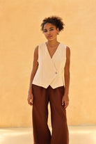 Woman wearing a sleeveless blazer and brown pants against a beige background