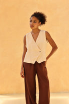 Woman wearing a beige sleeveless blazer over brown pants against a beige background
