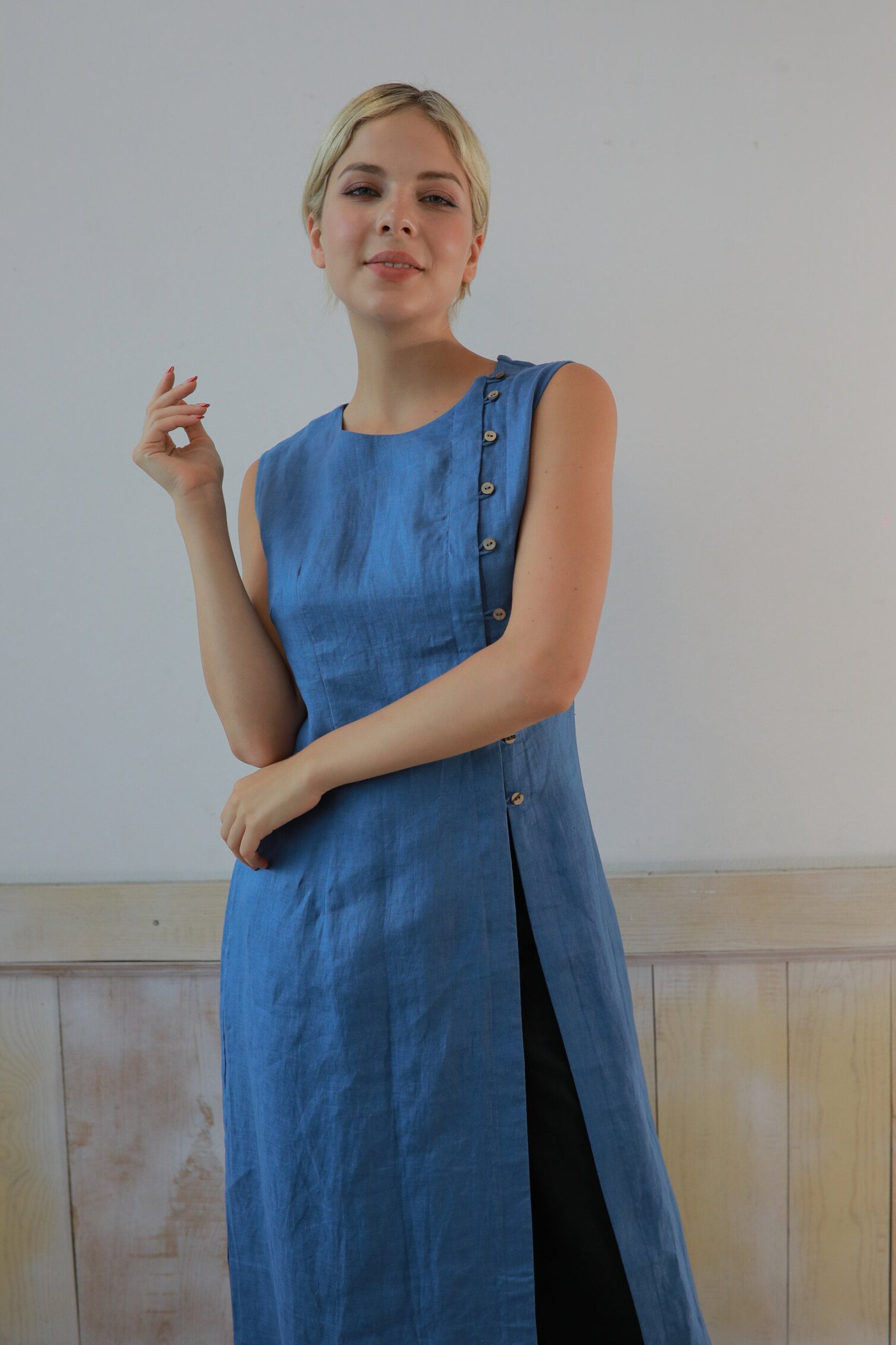Woman wearing a blue sleeveless dress with buttons against a plain background