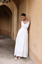 Woman in a white dress standing in an arched hallway with beige walls.