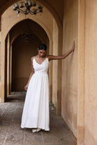 Woman in a white dress standing in an arched hallway with beige walls.