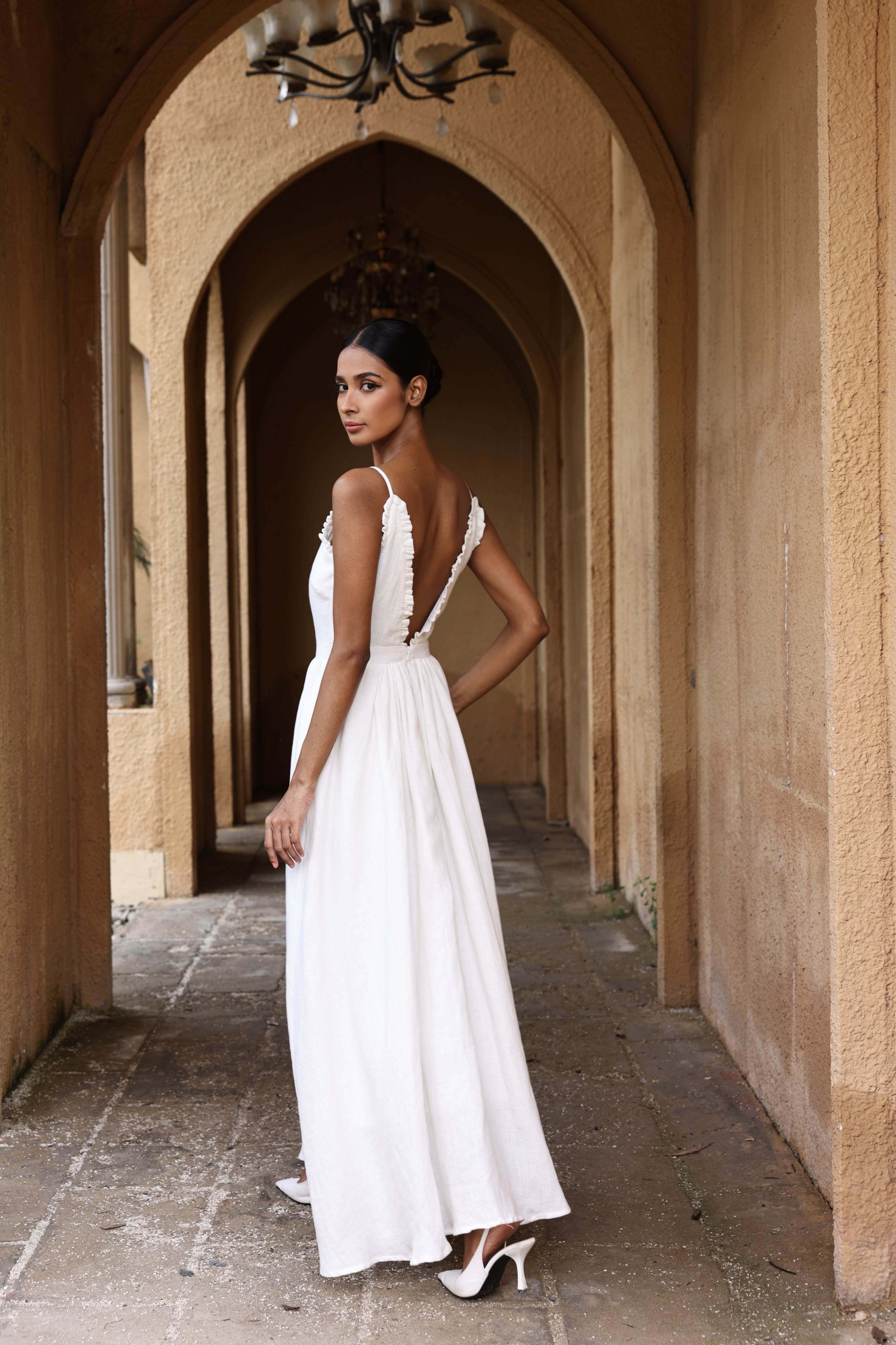 Woman in a white dress standing in an arched hallway with a chandelier.