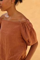 Person wearing a brown off-shoulder top against a beige background