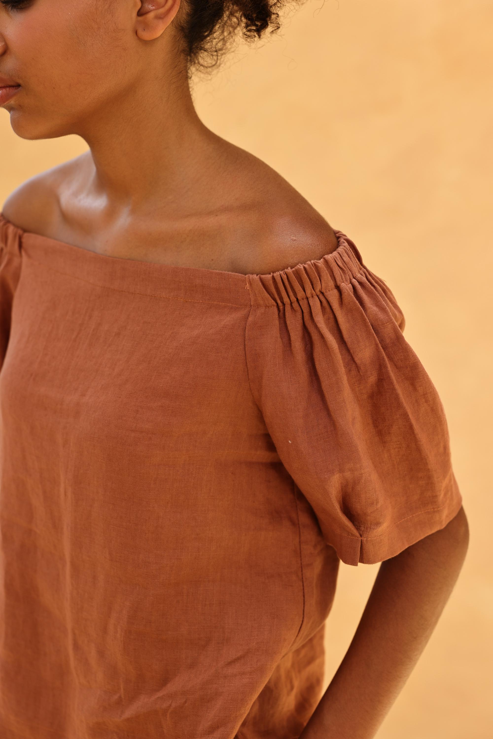 Person wearing a brown off-shoulder top against a beige background