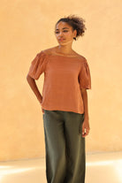 Woman wearing a rust-colored top and green pants against a beige background