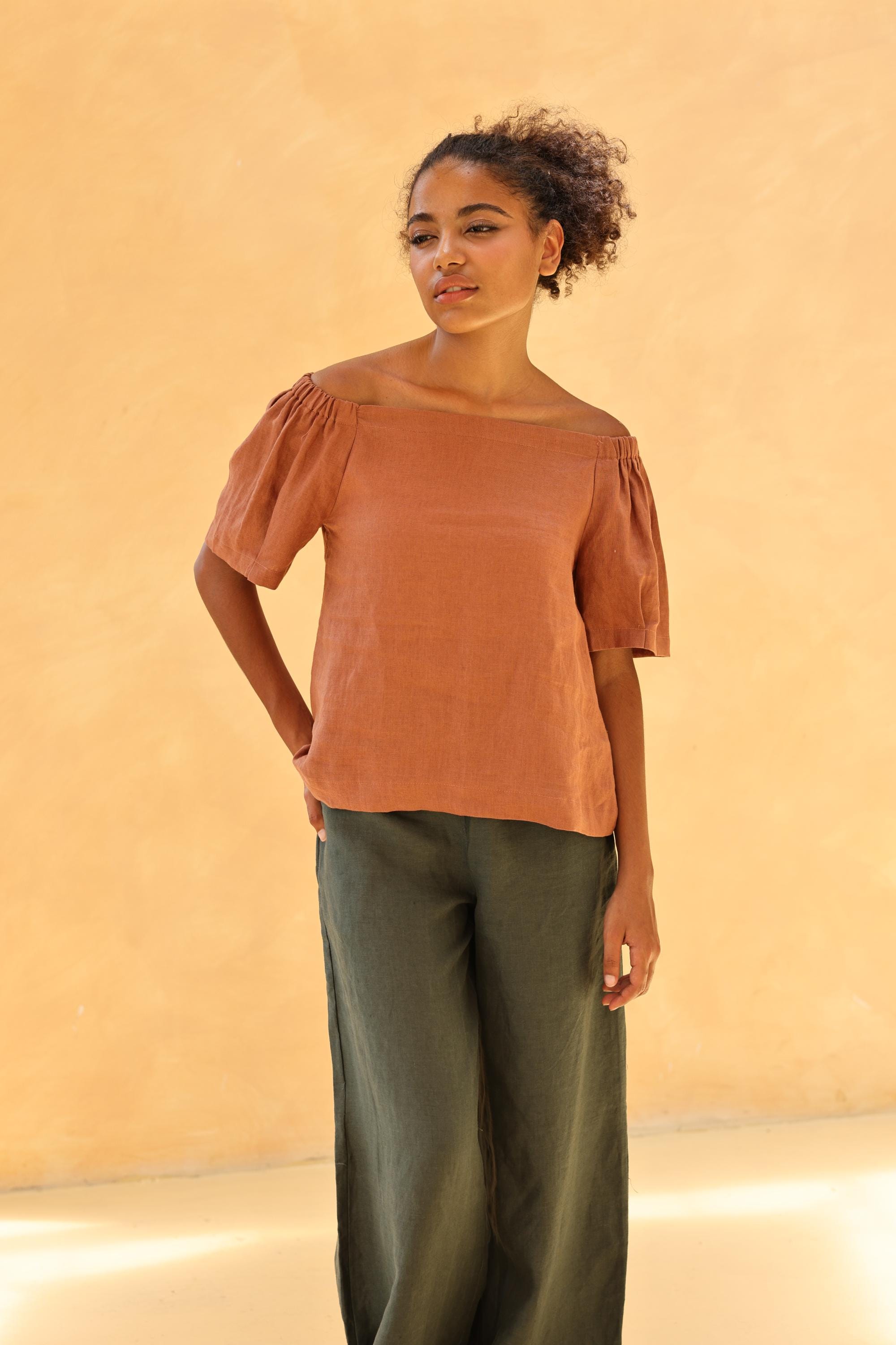Woman wearing a rust-colored top and green pants against a beige background