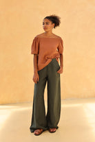 Woman wearing a rust-colored top and green pants against a beige background