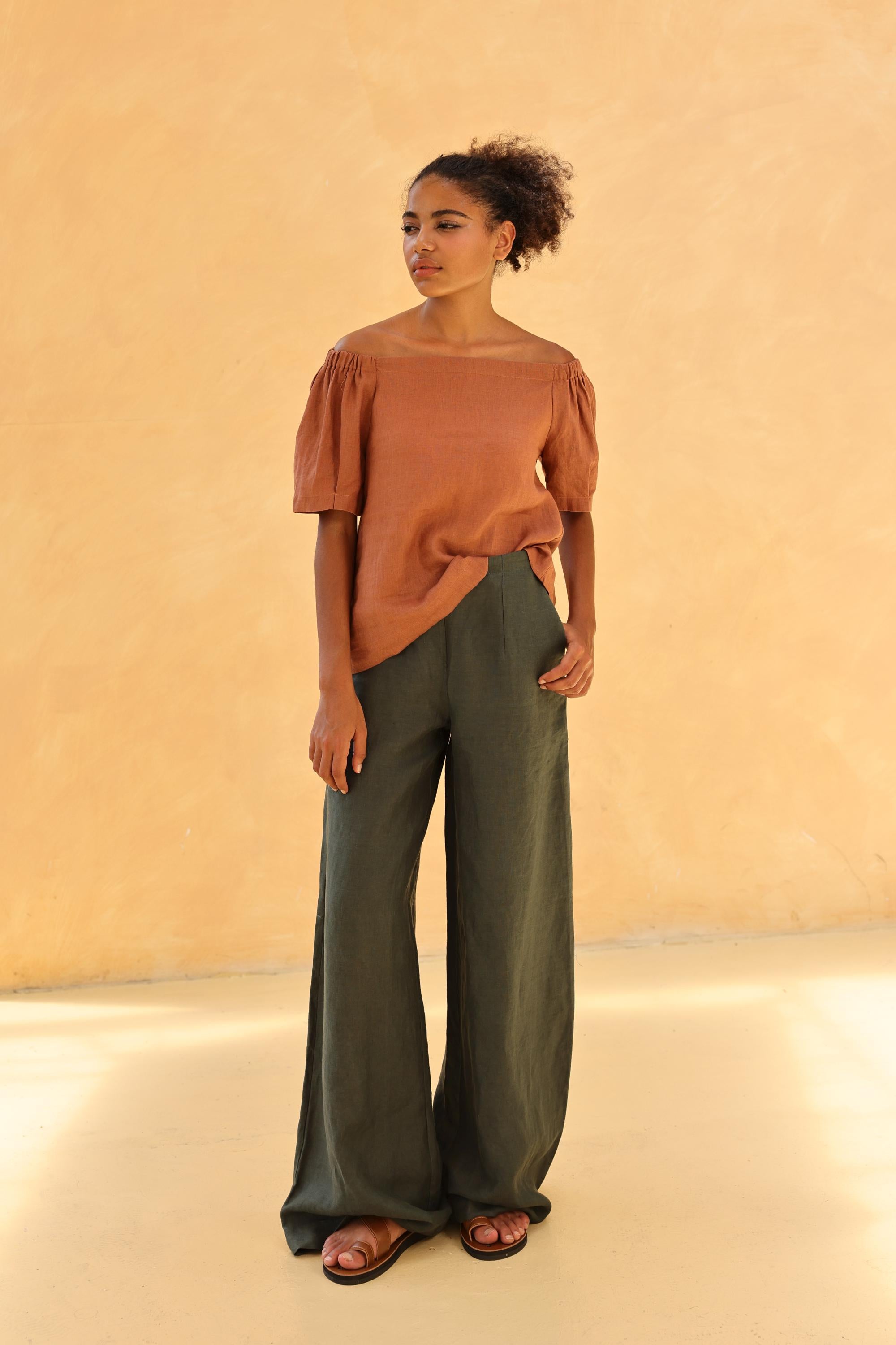 Woman wearing a rust-colored top and green pants against a beige background