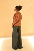 Person wearing a rust-colored top and green pants against a beige background