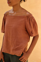 Person wearing a rust-colored off-shoulder top against a beige background