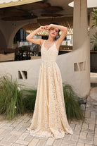 Woman in a beige lace dress standing in an outdoor setting with plants and architectural elements.