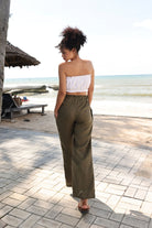 Woman in strapless top and wide-leg pants standing on a beach path with ocean view.