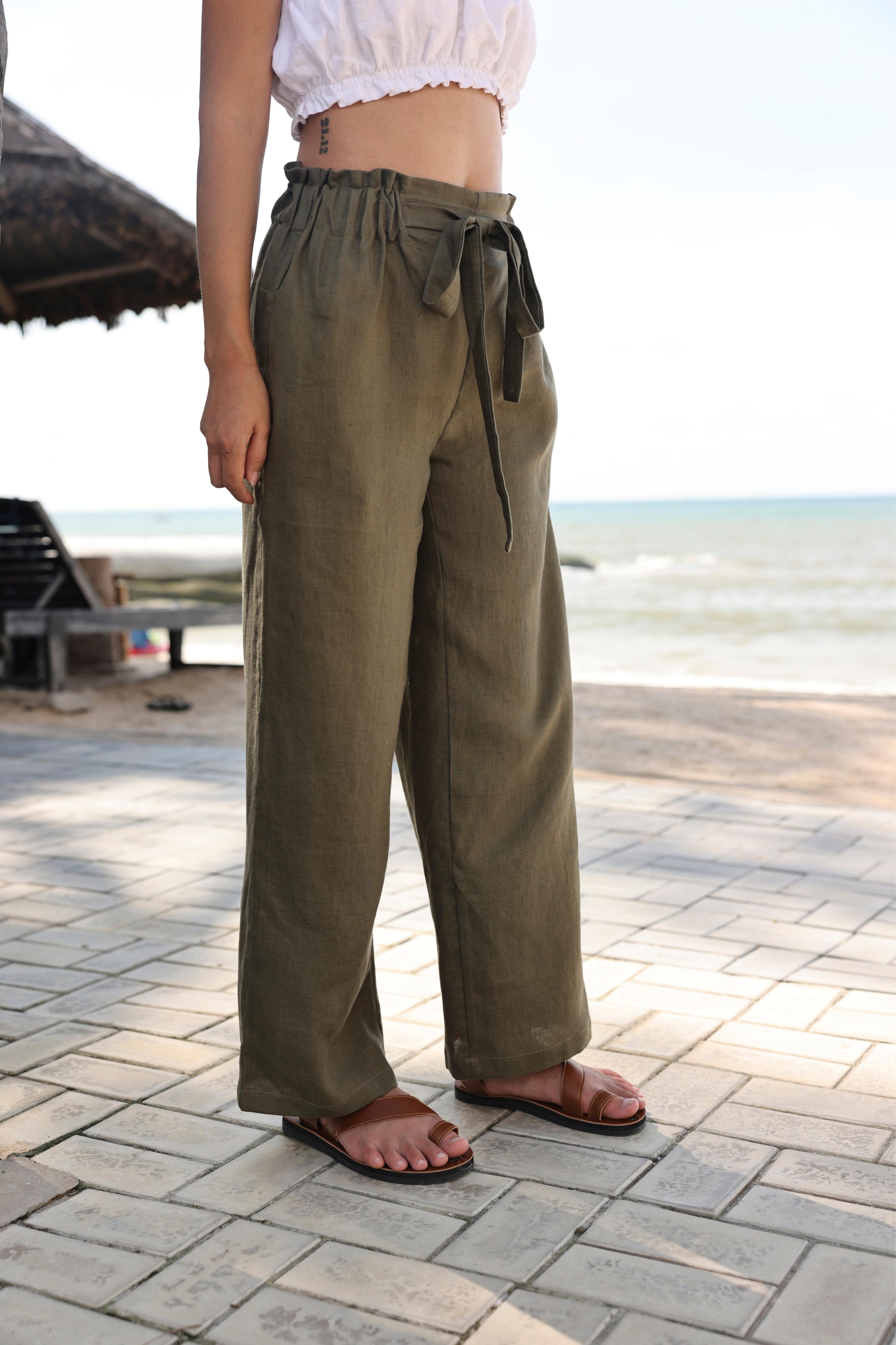 Person wearing olive green pants standing on a paved area with a beach in the background