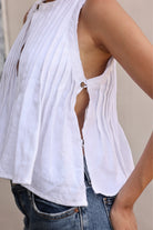 White sleeveless top with cut-out design worn by a person, with a neutral background.