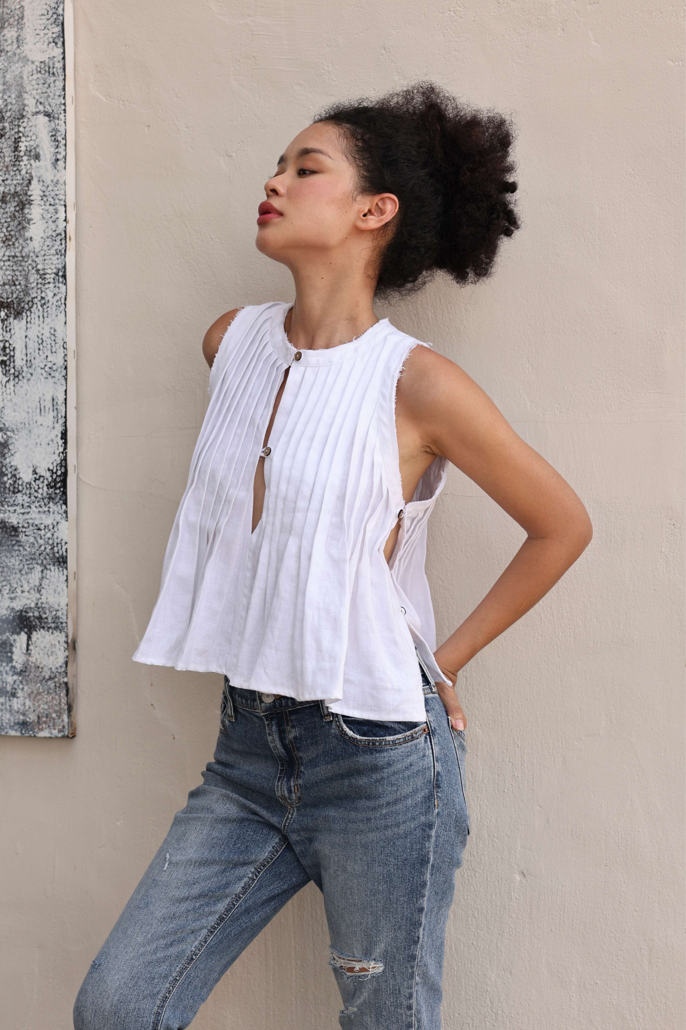 Woman wearing a white sleeveless top and blue jeans against a beige wall.