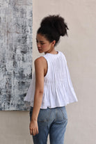 Woman wearing a white sleeveless top and blue jeans against a textured wall.