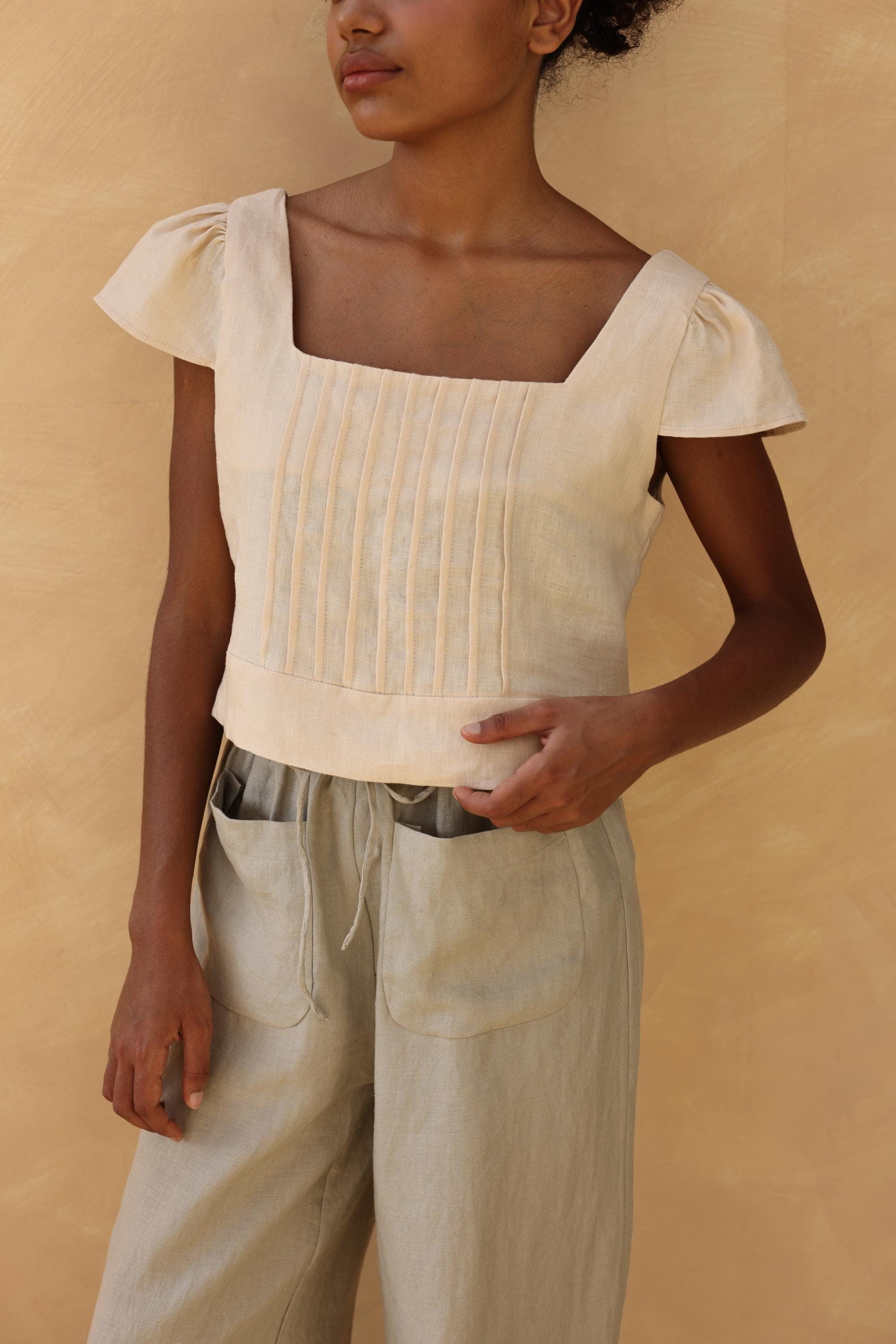 Woman wearing a beige top and pants against a beige background