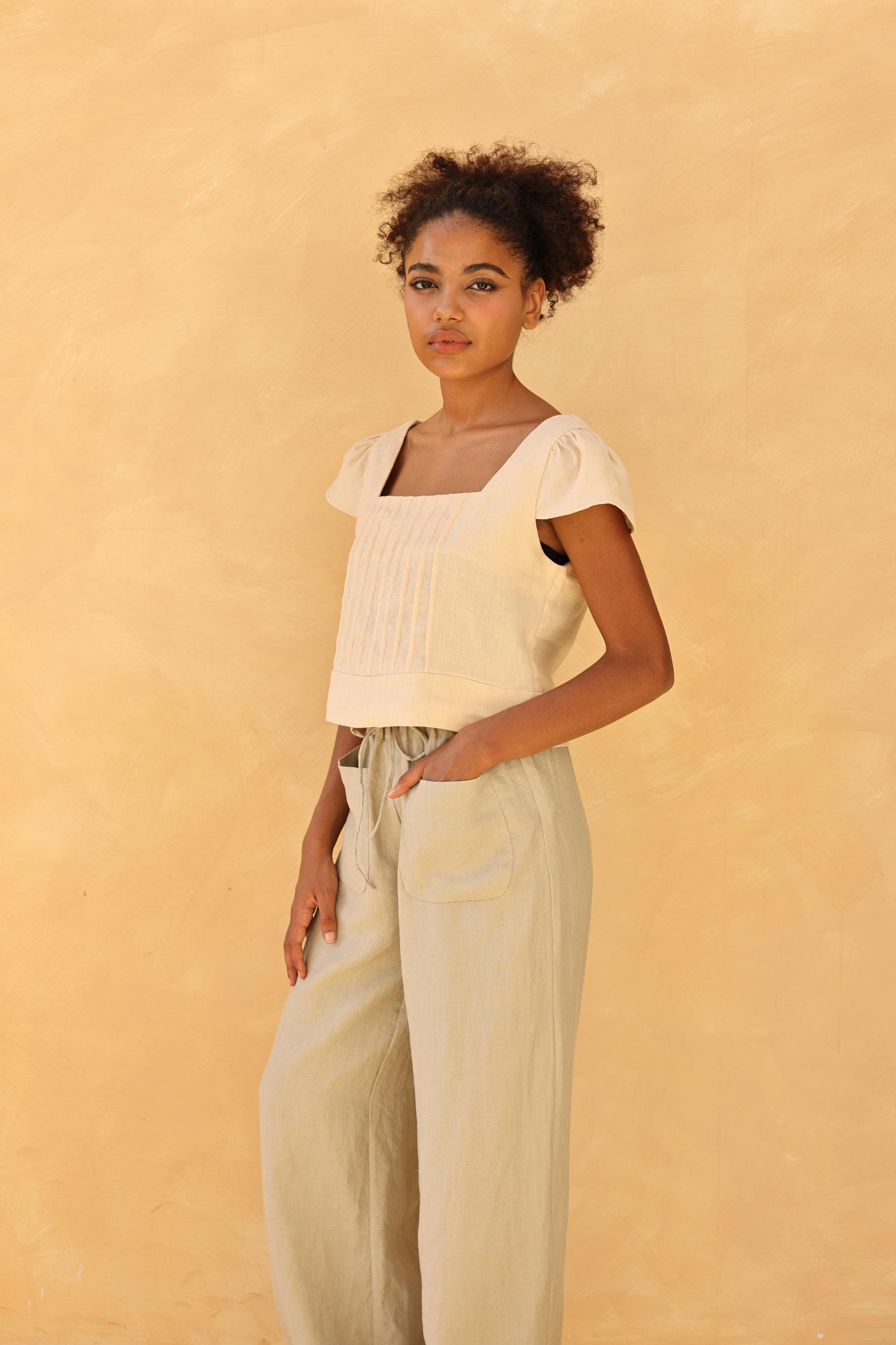 Woman wearing a top and beige pants against a beige background