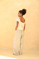 Woman wearing a light-colored top and beige pants against a beige background