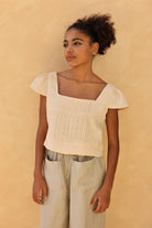 Woman wearing a light-colored top and pants against a beige background