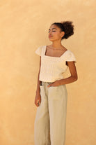 Woman wearing a light-colored top and pants against a beige background