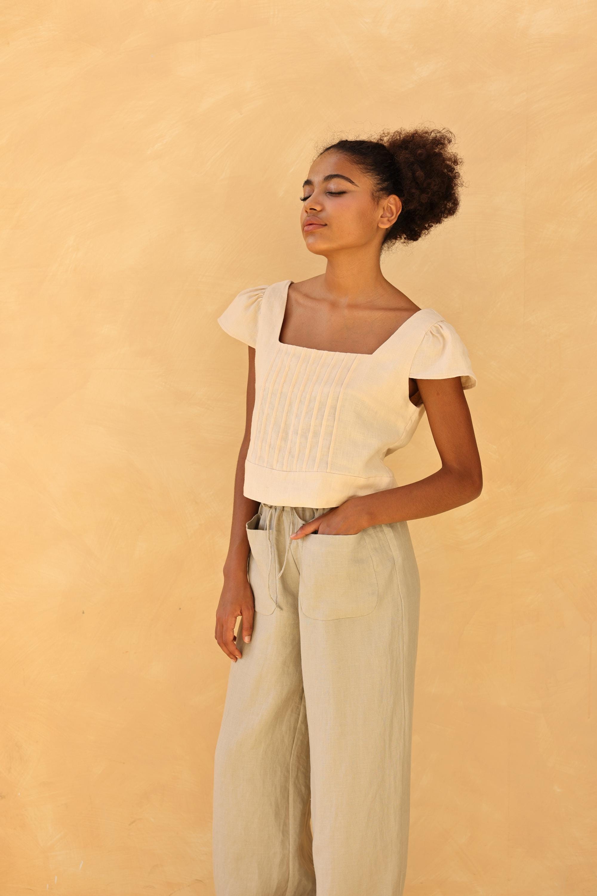 Woman wearing a light-colored top and pants against a beige background