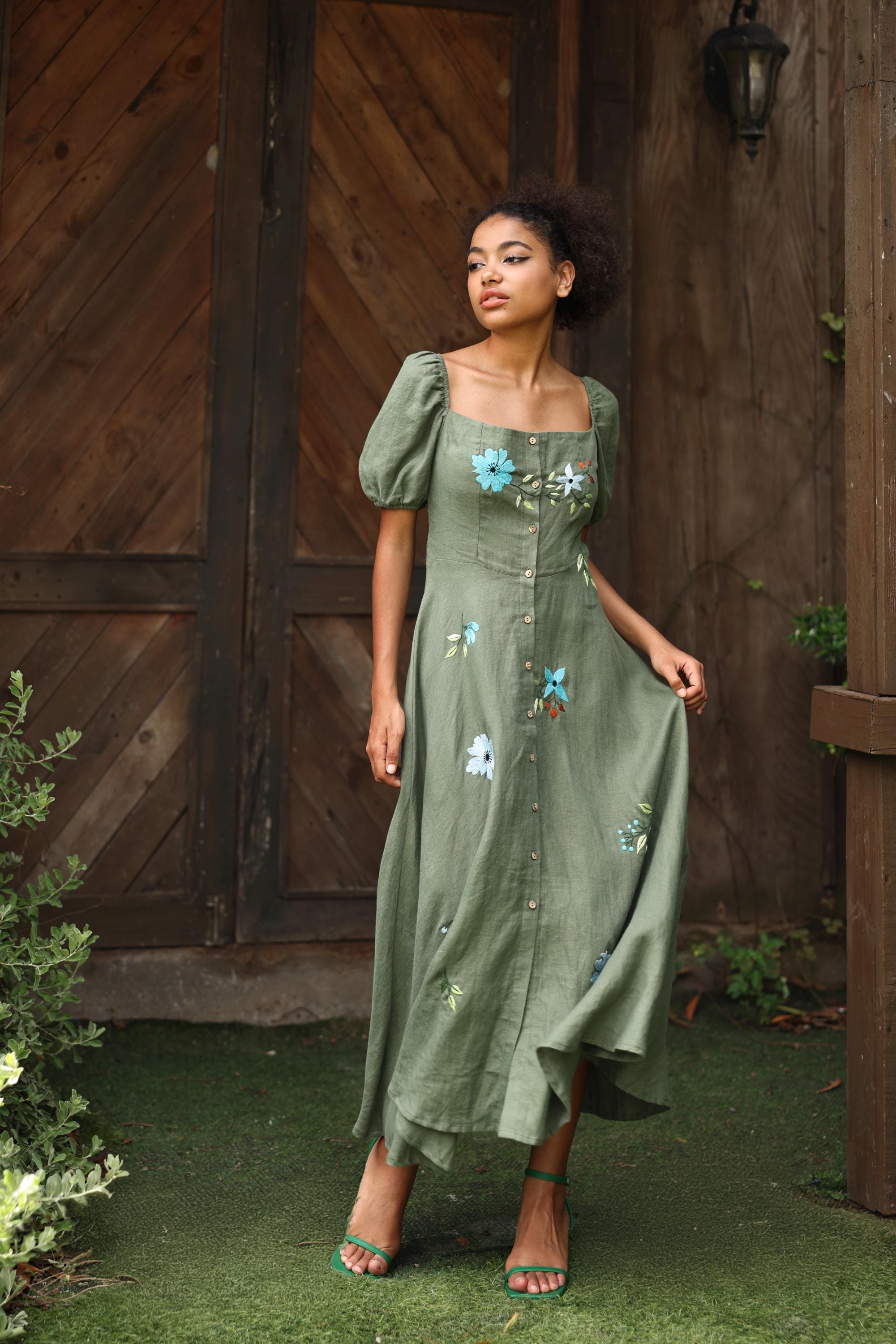 Woman in a green dress with floral embroidery standing in front of a wooden door.