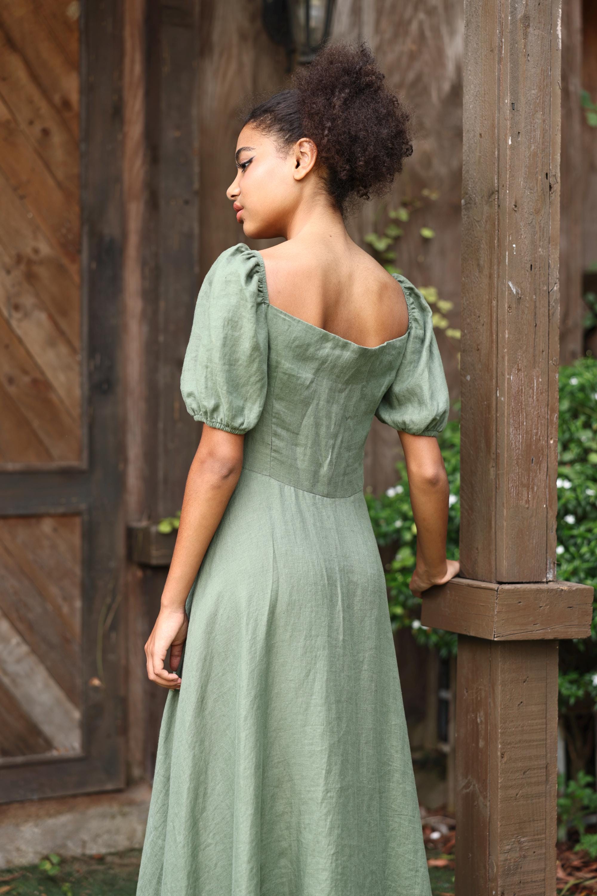 Woman in a green dress standing outdoors near wooden structures.