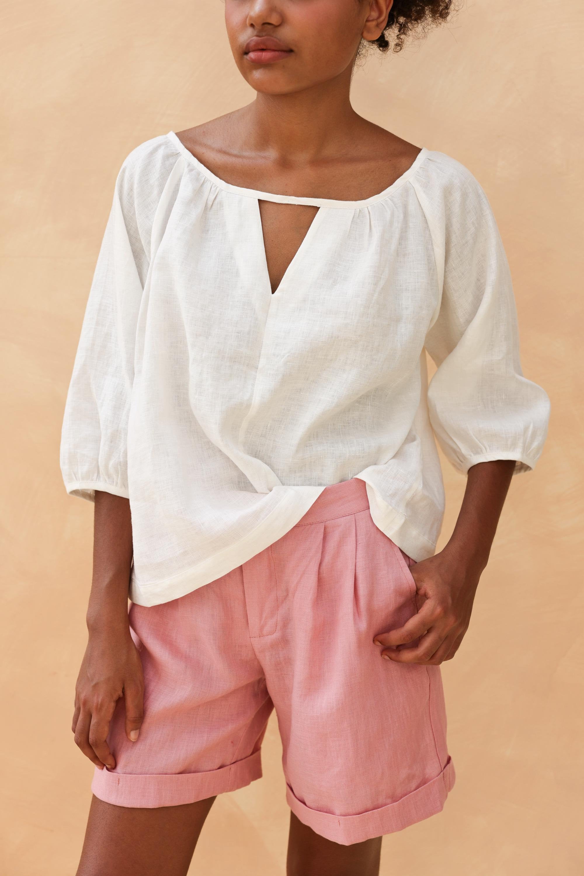 White puff sleeve linen top with a split neckline, styled with pink linen shorts.