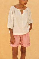 Person wearing a white top and pink shorts against a beige background