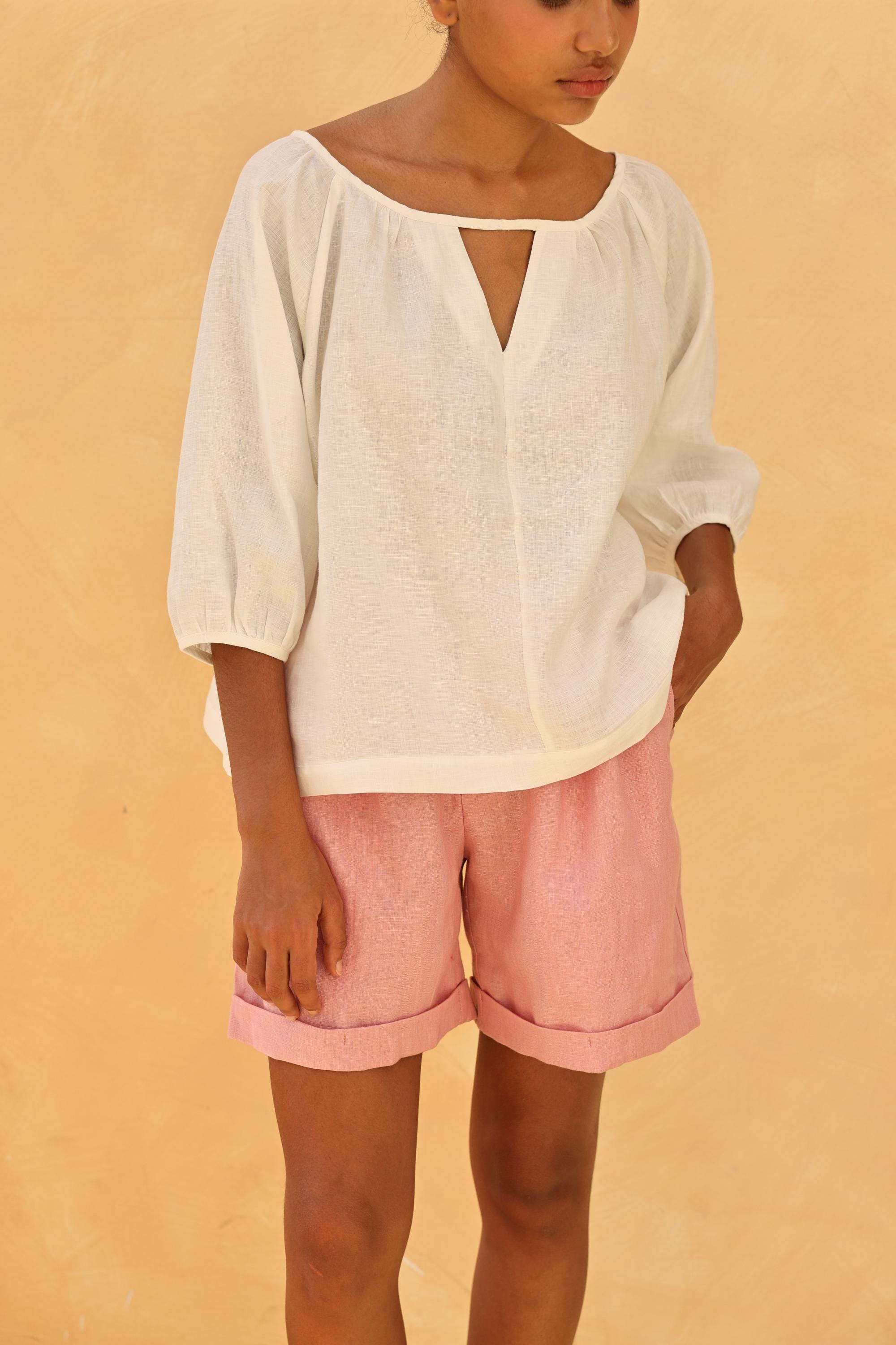 Person wearing a white top and pink shorts against a beige background