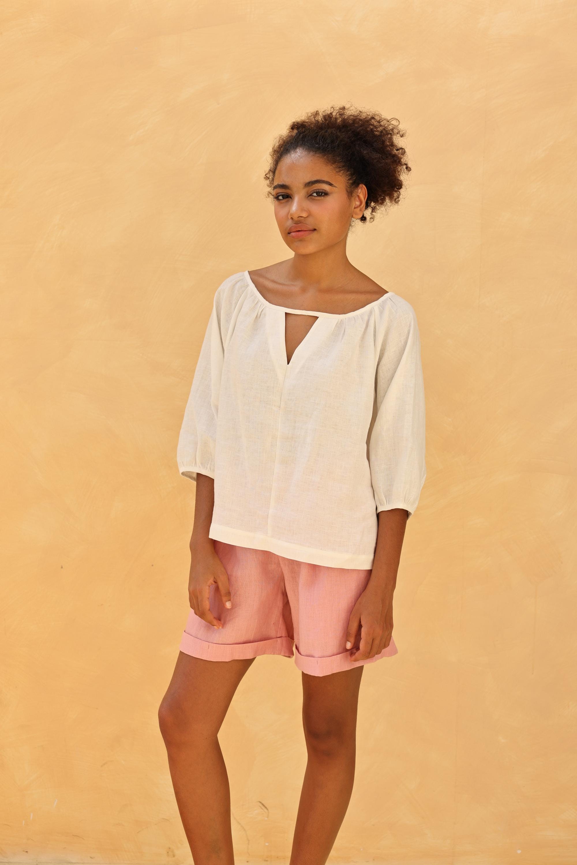 Woman wearing a white blouse and pink shorts against a beige wall