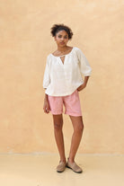 Woman wearing a white blouse and pink shorts against a beige background