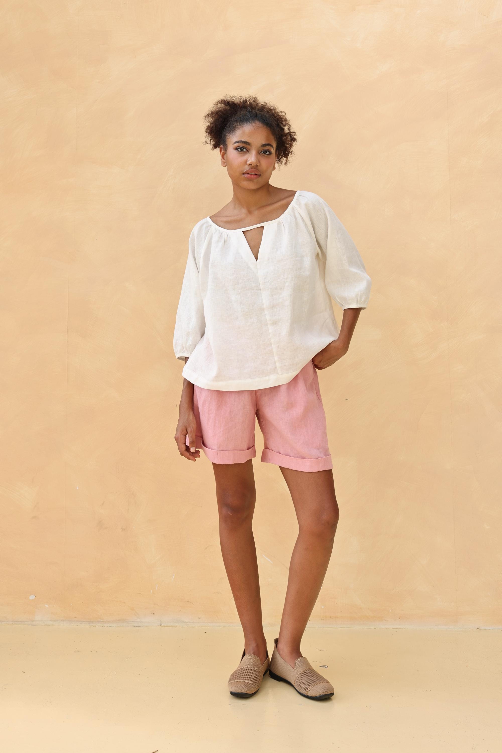 Woman wearing a white blouse and pink shorts against a beige background