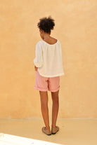 Person wearing a white top and pink shorts against a beige wall