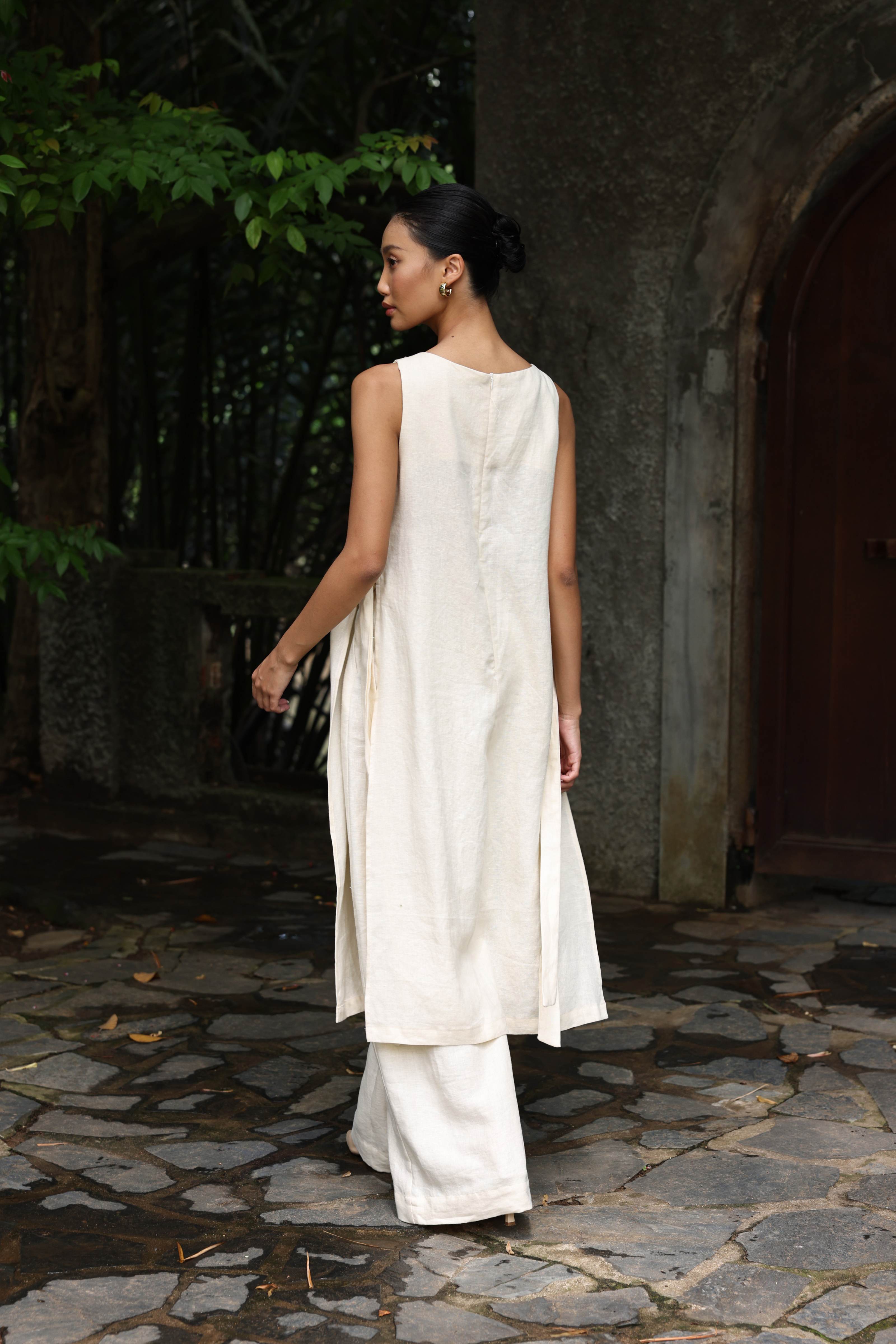 Woman in a white dress standing on a stone path with greenery in the background