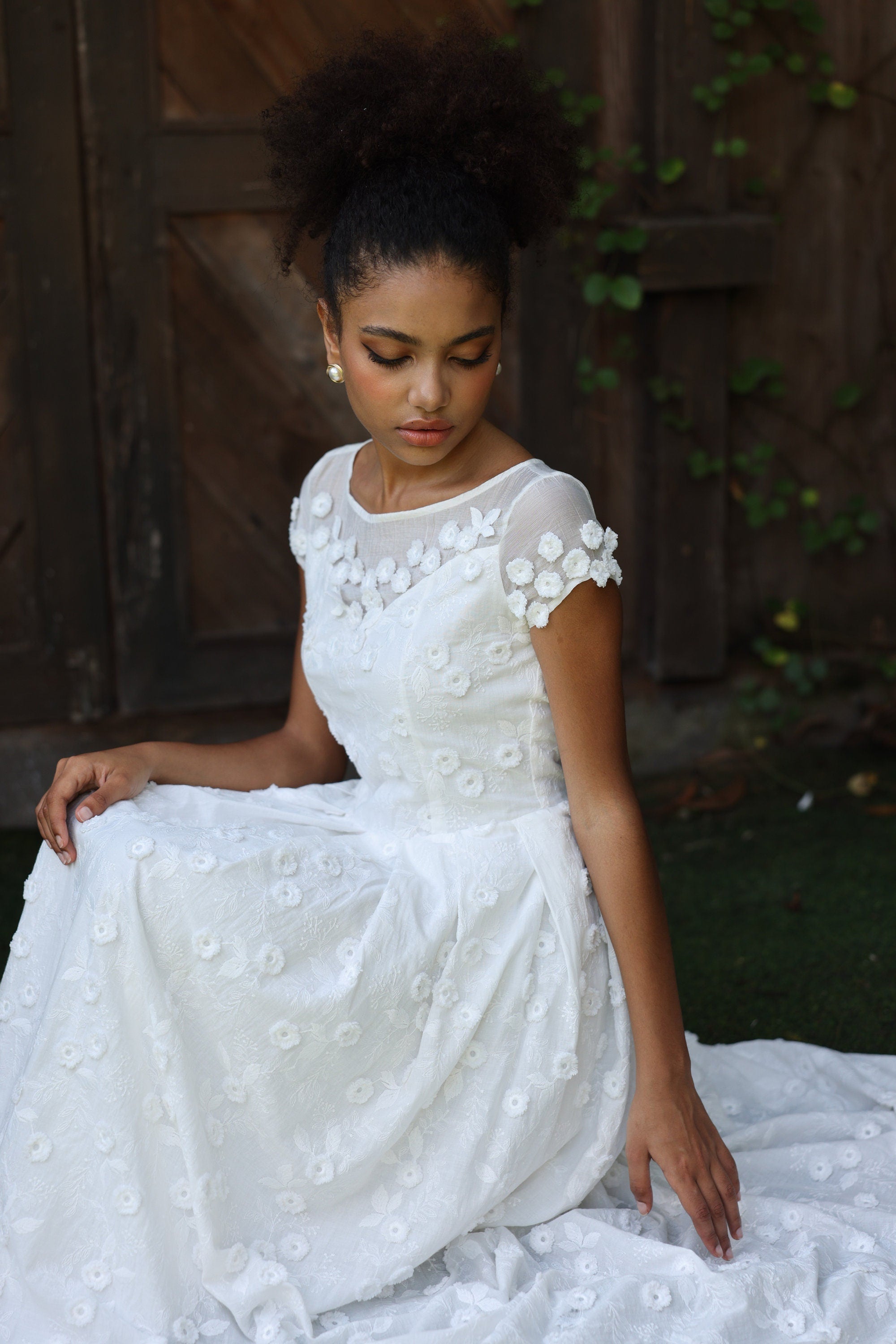 Woman in a white lace dress sitting outdoors with a wooden background